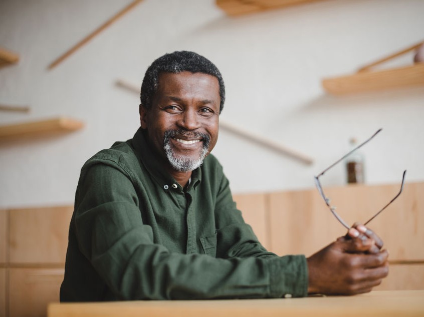older man holding glasses in hand smiling with teeth